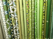 A photograph of different green textile rolls stacked vertically in a haberdashery shop.