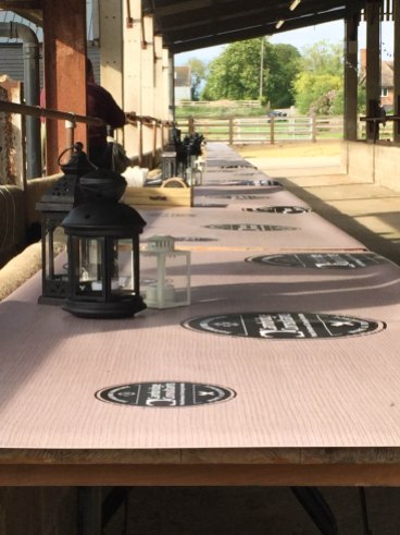 A photo of a line of trestle tables with napkins, cutlery and candles.