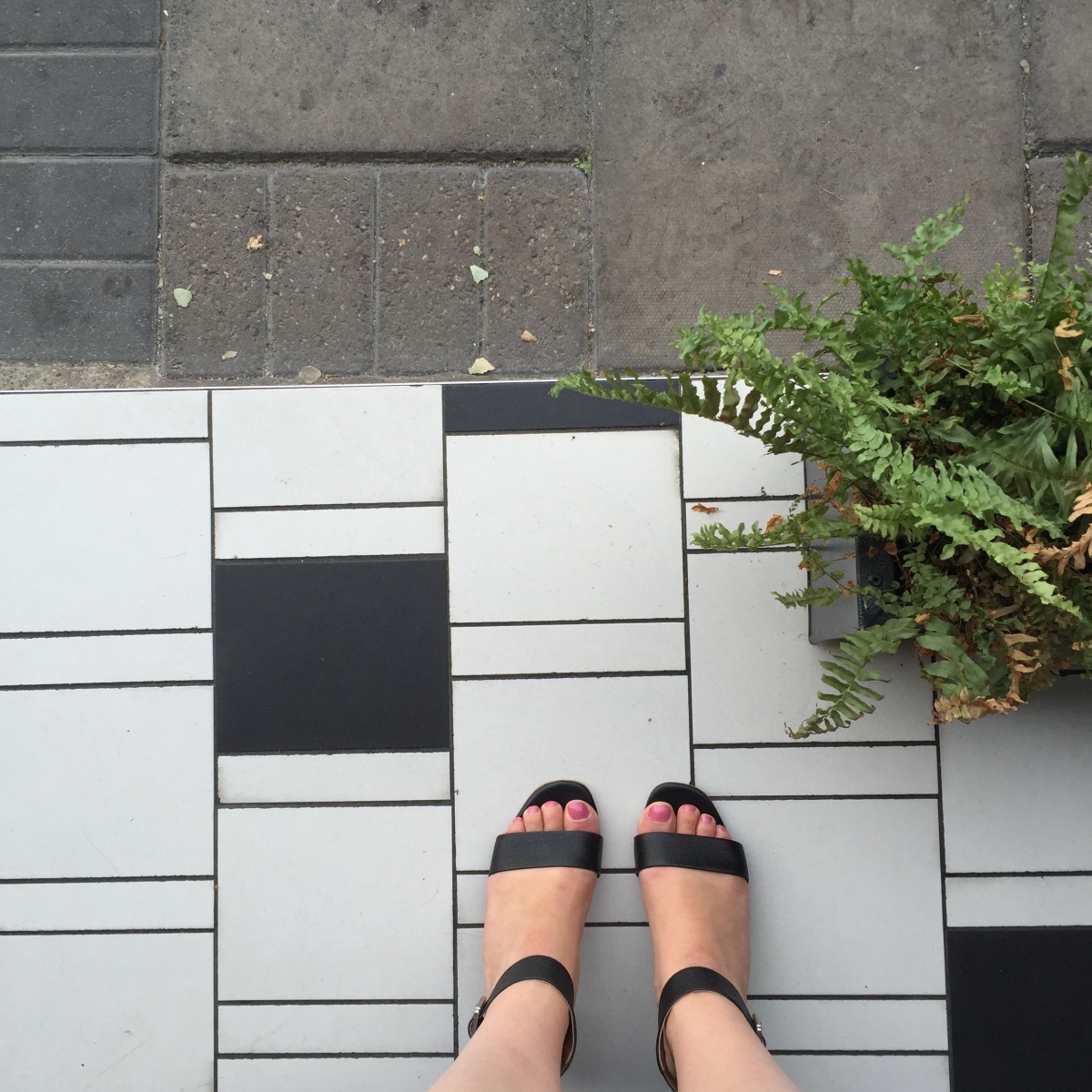 A top-down photograph of Emma's feet on the floor tiles outside NOVI that are at a different angle to the pavement slabs