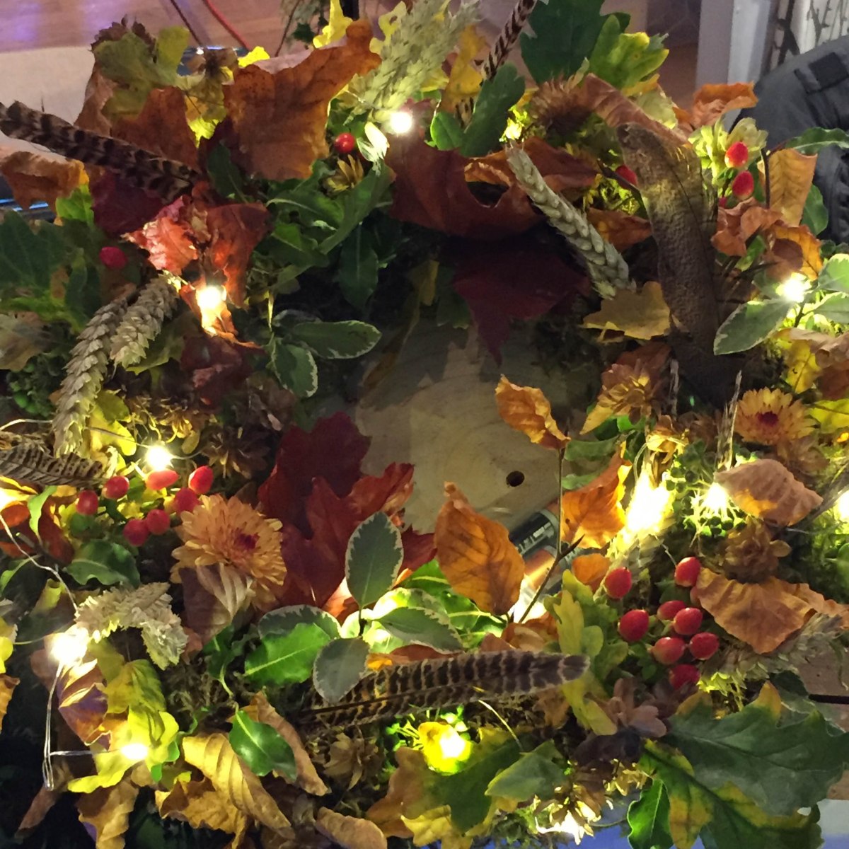 A photograph of a traditional-looking wreath with autumnal leaves, a few white fairy lights and even some game bird feathers