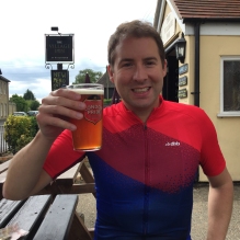 A photograph of Rob with a pint of London Pride sitting on a picnic-style bench outside the Village Inn in Witchford.